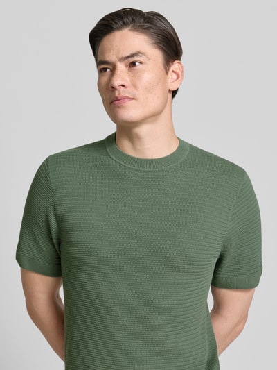 Männermodel trägt Strickshirt mit Rundhalsausschnitt Modell 'RILEY' von Jack & Jones Premium, grün, Strukturmuster, Reine Baumwolle, Slim-Fit, Nahaufnahme Oberkörper.