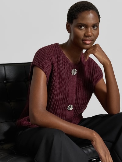 Kobiece modelka nosi Relaxed Fit kamizelkę dzianinową z dodatkiem wełny Model 'Norma' od b.young, Mieszanka materiałów, okrągły dekolt, krótkie rękawy, listwa guzikowa, długość tyłu w rozmiarze S: 52 cm, widok na górną część ciała z przodu.