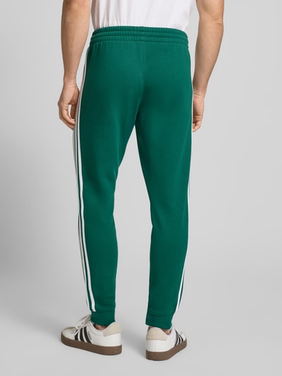 Männermodel trägt grüne Sweatpants mit elastischem Bund von adidas Originals, Baumwoll-Elasthan-Mix, lockerer Schnitt, Ganzkörperansicht Rückansicht.