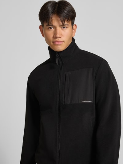 Männermodel trägt schwarze Fleecejacke mit Zweiwege-Reißverschluss Modell 'MASON' von JACK & JONES, Nahaufnahme Oberkörper, Regular Fit, Logo, Stehkragen, Eingrifftaschen.