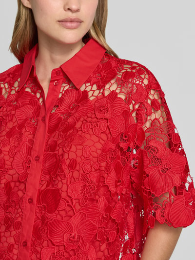 Frauenmodel trägt Regular Fit Bluse aus Spitze Modell 'GALA' von YAS in leuchtendem Rot mit floralen Mustern, Nahaufnahme Oberkörper.