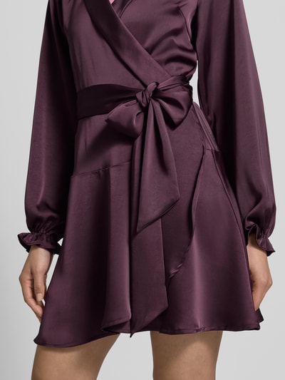 Frauenmodel trägt knielanges Kleid in Wickel-Optik Modell 'Colbie' von Neo Noir, Elastischer-Material-Mix, Satin, Taillenband, Nahaufnahme Oberkörper.