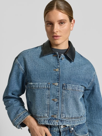 Vrouwenmodel draagt Cropped Jeansjacke aus reiner Baumwolle van Diesel in blauwe denim met knopen en steekzakken, regular fit, detailopname bovenlichaam, context: dames jeansjack van pure katoen, cropped, regular fit, doorknoopsluiting, opgestikte steekzakken, ruglengte maat S: 41 cm, borstbreedte maat S: 42 cm, mouwlengte maat S: 53 cm.
