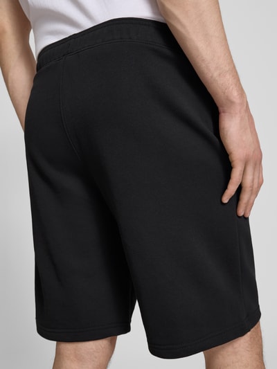 Männermodel trägt Bermudas mit elastischem Bund und Label-Stitching von CHAMPION, schwarze Baumwoll-Mix Shorts, Rückansicht Ganzkörperansicht.