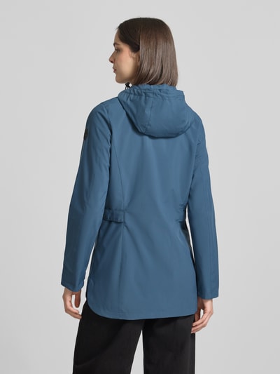 Frauenmodel trägt Regular Fit Regenmantel mit Logo-Detail von G.I.G.A. DX in Blau mit Kapuze, Zweiwege-Reißverschluss, Eingrifftaschen, Rückenlänge 76 cm, Schulterbreite 40 cm, Brustweite 50 cm, Ärmellänge 66 cm, Ganzkörperansicht Rückansicht.