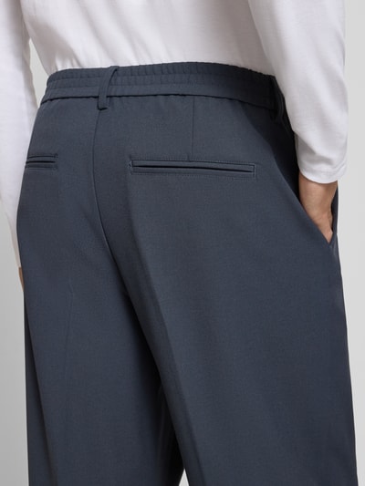 Männermodel trägt Straight Fit Hose mit Viskose-Anteil Modell 'Grant' von Casual Friday, dunkelblau, Teilelastikbund, Detailaufnahme, KI-modifiziertes Bild. Elastischer Material-Mix, Bügelfalten, Knopf- und Reißverschluss, Bundweite 43 cm, Innenbeinlänge 74 cm.