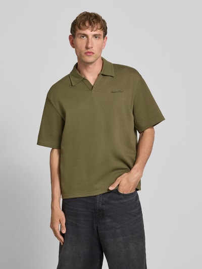 Männermodel trägt Regular Fit poloshirt met logo model 'Eddie' van Redefined Rebel, katoenmix, V-hals, olijfgroen, ruglengte maat M 73 cm, ganzkörperansicht van voren.