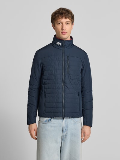 Männermodel trägt Regular Fit Jacke mit Stehkragen von Helly Hansen in Dunkelblau mit Logo-Print, Reißverschluss und Eingrifftaschen, Ganzkörperansicht von vorne. Rückenlänge 70 cm, Schulterbreite 46 cm, Brustweite 54 cm, Ärmellänge 69 cm, Größe M.
