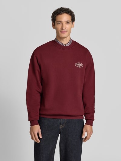 Männermodel trägt Sweatshirt mit Logo-Print Modell 'Worldwide' von Les Deux in Dunkelrot, Baumwoll-Mix, Ganzkörperansicht von vorne.