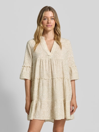 Vrouwenmodel draagt Ausgestelltes Blusenkleid aus reiner Baumwolle Modell 'DICTHE' van Vero Moda, lichtbeige all-over patroon, mini lengte, henley hals, trompet mouwen, katoen, aangerimpeld, frontale bovenlichaam close-up.