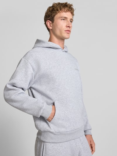 Männermodel trägt Regular Fit Hoodie aus Baumwoll-Mix von REVIEW in Hellgrau mit Känguru-Tasche, elastischen Abschlüssen, Ganzkörperansicht von vorne.