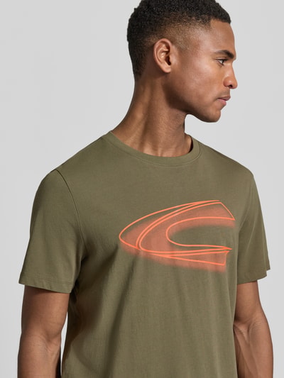 Männermodel trägt Regular Fit T-Shirt aus reiner Baumwolle von camel active in Olivgrün mit Label-Print, Nahaufnahme Oberkörper.