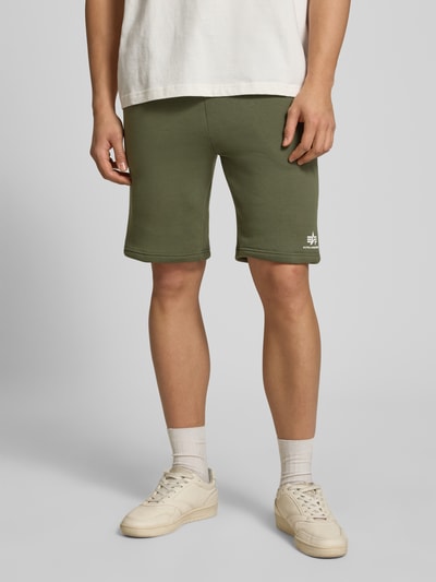 Männermodel trägt Shorts mit Eingrifftaschen und Logo-Print von Alpha Industries in Olivgrün, Baumwoll-Mix, Nahaufnahme Oberschenkel bis Füße.