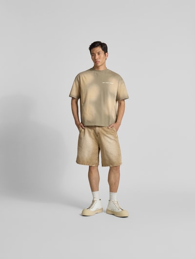 Männermodel trägt T-Shirt mit Label-Print von Don´t Waste Culture, beige Farben, Reine Baumwolle, Gerader-Schnitt, Ganzkörperansicht von vorne.