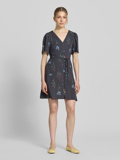 Frauenmodel trägt Leicht ausgestelltes Minikleid aus reiner Viskose Modell 'ALBA' von Vero Moda in Dunkelgrau, floral gemustert, Taillengürtel, V-Ausschnitt, Kurzarm, Mini-Länge, Ganzkörperansicht von vorne