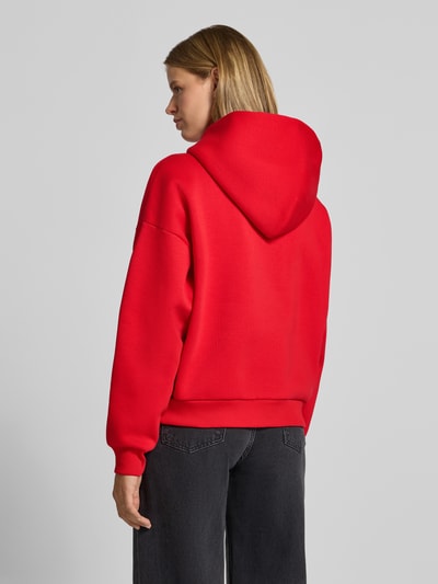 Frauenmodel trägt Kapuzenpullover aus Baumwoll-Mix von REVIEW in Rot mit lockerer Passform, gerippten Bündchen, Ganzkörperansicht Rückansicht.