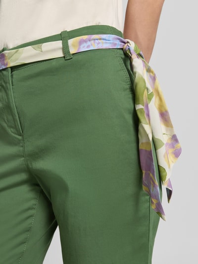 Kobieta nosi Slim Fit Chino mit Viskose-Anteil od Christian Berg Woman, zielony kolor, materiał elastyczny, pasek z tkaniny, zbliżenie na biodra.