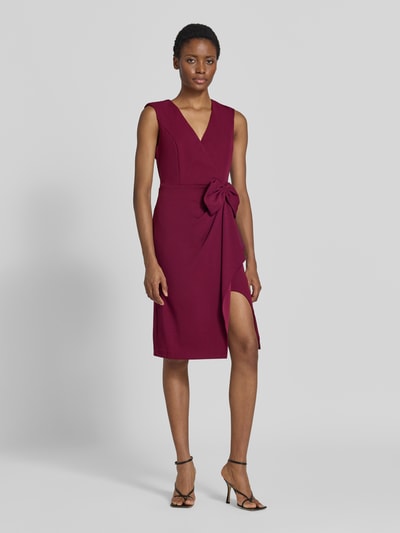 Frauenmodel trägt Knielanges Kleid mit Zierschleife von Adrianna Papell in Dunkelrot, ärmellos, tailliert, Wickel-Optik, Ganzkörperansicht von vorne.