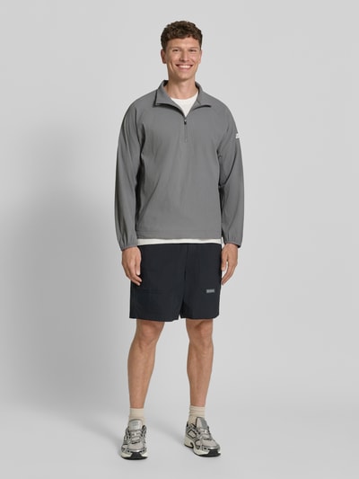 Männermodel trägt Regular Fit Sweatshirt mit Strukturmuster von EA7 Emporio Armani in Grau, Reißverschluss, Logo-Patch, Ganzkörperansicht von vorne.