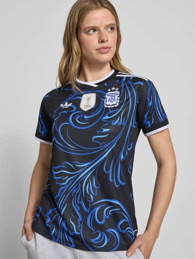 Frauenmodel trägt Argentinien Auswärtstrikot 2026 von adidas Sportswear, mehrfarbig, Regular Fit, Logo-Stitching, V-Ausschnitt, Sweat-Material, Ganzkörperansicht von vorne.