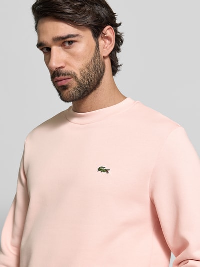 Männermodel trägt Classic Fit Sweatshirt aus katoenmix van Lacoste in effen lichtroze, logo-stitching op borst, crew neck, lange mouw, close-up bovenlichaam.