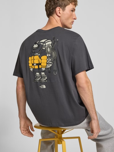 Männermodel trägt T-Shirt aus reiner Baumwolle Modell 'Gear Up Get Out' von The North Face, Logo-Print auf dunklem Stoff, Ganzkörperansicht Rückansicht, Regular Fit, kurzärmlig, Rundhalsausschnitt, Rückenlänge bei Größe M: 68 cm.