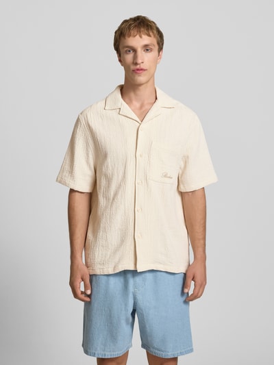 Męski model nosi Regular Fit Freizeithemd mit Logo-Stitching od REVIEW z czystej bawełny, kremowy, krój regular fit, kołnierz rewersowy, zapięcie na guziki, półrękaw, kieszeń na piersi, logo na kieszeni, długość tyłu w rozmiarze M: 68 cm, szerokość w rozmiarze M: 55 cm, długość rękawa w rozmiarze M: 27 cm, faktura o wyraźnej strukturze, zdjęcie całości sylwetki od przodu