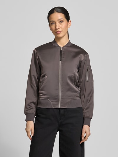 Modelka kobieta ma na sobie Regular Fit Bomberjacke mit Stehkragen Modell 'Beth' od khujo w kolorze ciemnoszarym, gładka tekstura, kieszenie, elastyczne mankiety, widok całej sylwetki z przodu, krój regular fit, długość tyłu w rozmiarze S: 54 cm, szerokość ramion w rozmiarze S: 46 cm, szerokość w biuście w rozmiarze S: 47 cm, długość rękawa w rozmiarze S: 58 cm.