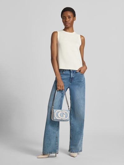 Frauenmodel trägt Shoulder Bag mit Logo-Detail Modell 'Ruby' von GUESS in Denim-Optik mit Überschlag, Ganzkörperansicht von vorne.