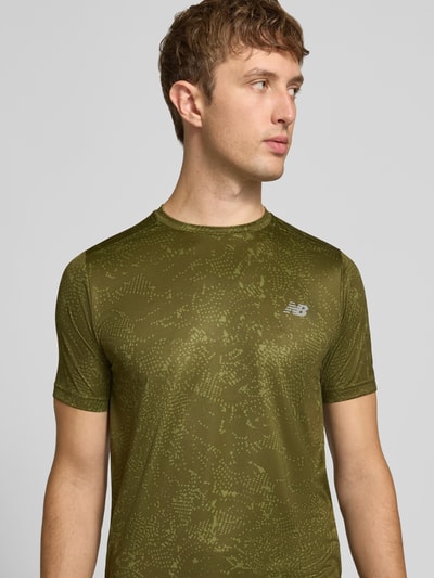 Männermodel trägt T-Shirt mit Logo-Print Modell 'ESSENTIAL' von New Balance in Olivgrün mit grafischer Textur, Nahaufnahme Oberkörper, gerader Schnitt, Rundhalsausschnitt, Rückenlänge bei Größe M 70 cm.