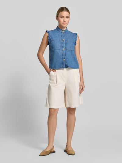 Frauenmodel trägt Regular Fit Hemdbluse in Denim-Optik von More & More aus reiner Baumwolle, Stehkragen mit Rüschenbesatz, Brusttaschen, ärmelloses Design, durchgehende Knopfleiste, Rückenlänge bei Größe 36: 50 cm, Ganzkörperansicht von vorne.