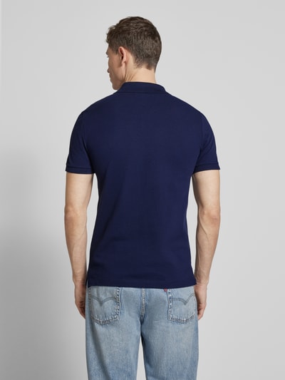Męski model nosi Slim Fit Poloshirt aus reiner Baumwolle von Lacoste, efekt: jednolity kolor, krój slim fit, wyhaftowane logo, kołnierzyk polo, krótki rękaw, zakończenie rękawów: prążkowane, wykończenie: z rozcięciami po bokach, wykończenie materiału: pika, materiał: bawełna; zdjęcie: widok całej sylwetki od tyłu.