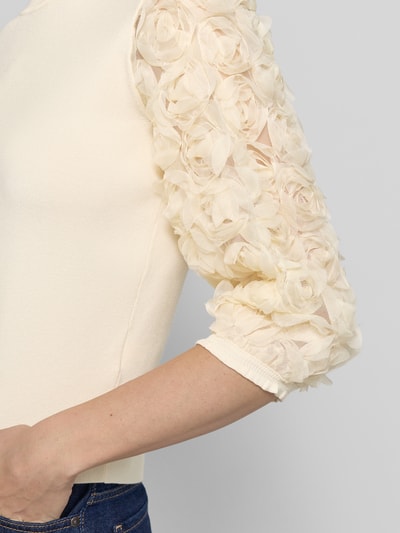 Kobieta nosi Strickshirt aus Viskose-Mix mit floralen Applikationen od Zero, kremowy kolor, dopasowany krój, okrągły dekolt, detal rękawa, damska moda, długość tyłu 48 cm, długość rękawa 43 cm, zbliżenie na górną część ręki