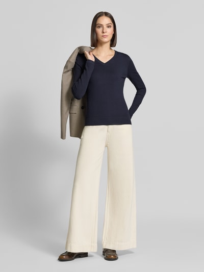 Vrouwenmodel draagt Pullover uit Viscosemix met V-hals van Christian Berg Woman, recht model, ribboorden, ruglengte maat S 46 cm, mouwlengte maat S 63 cm, donkerblauw, wijde crèmekleurige broek, bruine schoenen, Ganzkörperansicht von voren.