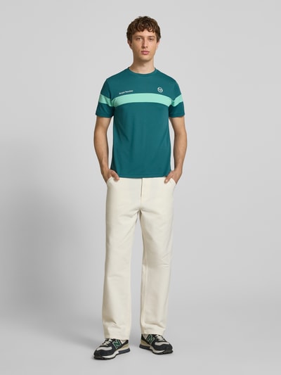 Männermodel trägt Regular Fit T-Shirt mit Logo-Print Modell 'Leone' von SERGIO TACCHINI in Türkis mit Rundhalsausschnitt, Rückenlänge 71 cm, Ganzkörperansicht von vorne.