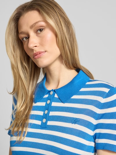 Vrouwenmodel draagt Regular Fit Poloshirt uit Lyocell-Seiden-Mix van Tommy Hilfiger met blauw-wit allover-streep, logo-stiksel, fijngebreide textuur, polokraag, korte knoopsluiting en geribde korte mouwen, Nahaufnahme bovenlichaam.