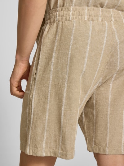 Männermodel trägt Leinenshorts mit Logo-Stitching von REVIEW, beiger Baumwoll-Mix mit weißen Streifen, strukturierte Textur, Nahaufnahme Rückansicht.