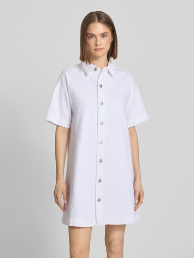 Frauenmodel trägt Loose Fit Jeanskleid aus Baumwoll-Mix Modell 'SKY' von Pieces in Weiß mit Knopfleiste, Denim-Optik, Mini-Länge, Hochgeschlossen, überschnittene Schultern, Kurzarm, gerader Saum, Ganzkörperansicht von vorne.