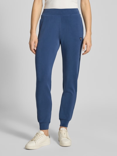 Kobiece modelka nosi Sweatpants mit Label-Detail od Guess Activewear, niebieski kolor, prosty krój, elastyczny materiał, z kieszeniami, całkowity widok z przodu.