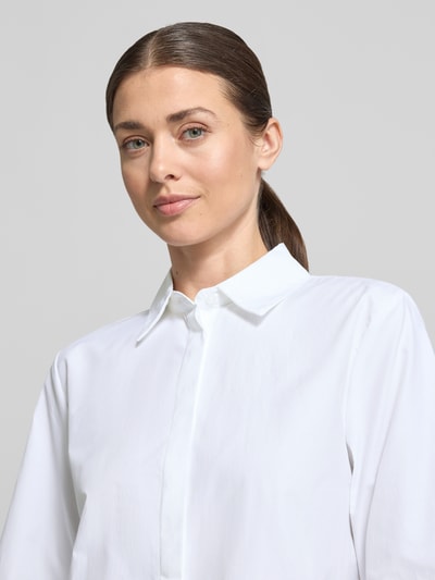 Kobiece modelka nosi bluzkę koszulową Regular Fit Hemdbluse im Halbarm-Design model 'Netti' von Soyaconcept, mieszanka bawełny, krój regular fit, kołnierzyk koszulowy, rękaw o dł. 1/2, biały kolor, gładka tekstura. Zbliżenie na górną część ciała z przodu.