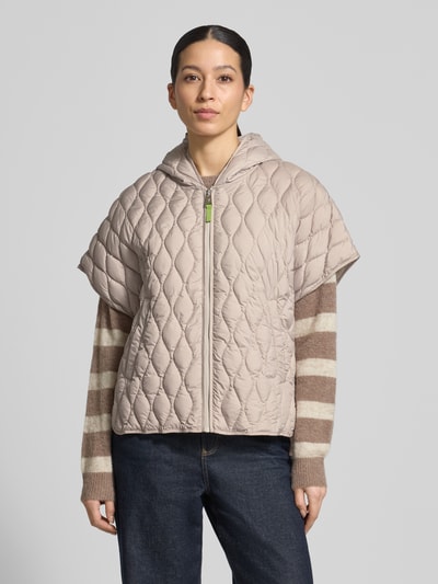 Frauenmodel trägt Steppjacke im kurzärmeligen Design von Fuchs Schmitt in Beige, lockerer Schnitt mit Kapuze, Reißverschluss und Eingrifftaschen, Struktur durch gesteppte Rauten, Kombi mit gestreiftem Pullover und Jeans, Ganzkörperansicht von vorne. Rückenlänge 65 cm, Schulterbreite 47 cm, Brustweite 57 cm (Größe 36).