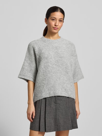 Modelka nosi szary Strickpullover mit gerippten Abschlüssen Modell 'ZOLLY' od American Vintage, luźny krój, miks wełny z alpaką, okrągły dekolt, półrękaw, długość tyłu w rozmiarze XS/S: 60 cm, długość rękawa: 33 cm, widok całej sylwetki z przodu.