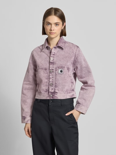 Frauenmodel trägt Regular Fit Jeansjacke mit Logopatch Modell 'Arca' von Carhartt Work In Progress in Violett, Reine Baumwolle, Eingrifftaschen, Umlegekragen, Knopfleiste, Ganzkörperansicht von vorne, Rückenlänge 50 cm, Schulterbreite 41 cm, Brustweite 51 cm, Ärmellänge 61 cm.