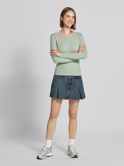 Frauenmodel trägt Regular Fit Langarmshirt aus Baumwoll-Mix Modell 'RILEY' von ONLY in Hellgrün zu Jeansrock, Ganzkörperansicht von vorne, Damen Langarmshirt von ONLY.