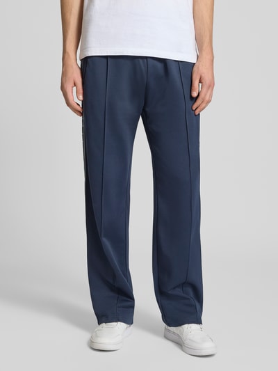 Männermodel trägt dunkelblaue Trainingshose mit Biese, aufgesetztem Band und Logo-Bestickung von REVIEW, Nahaufnahme Unterkörper, Regular Fit.