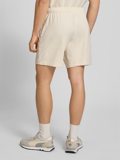 Männermodel trägt Shorts mit Logo-Stitching von PUMA PERFORMANCE in Beige mit Strukturmuster, elastischem Bund, geradem Schnitt, Ganzkörperansicht Rückansicht.