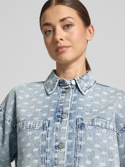 Kobieta nosi Oversized Jeansbluse mit Alpaka-Anteil od Armani Exchange z elastyczną mieszanką materiałów, nadruk z logo na całej powierzchni, kołnierzyk koszulowy, kieszenie na piersi, kolor niebieski, tekstura denim, widok na górną część ciała, z przodu.
