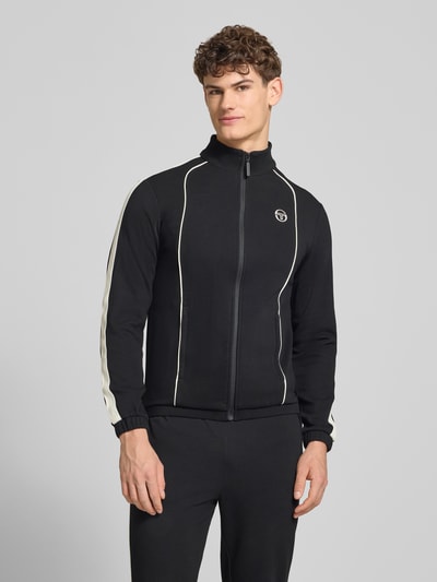 Männermodel trägt Slim Fit Tracksuit mit Logo-Stitching Modell 'Egeo' von SERGIO TACCHINI in Schwarz mit weißen Details, Nahaufnahme Oberkörper. Elastischer Baumwoll-Mix, Stehkragen, Reißverschluss, elastische Abschlüsse, körpernahe Passform.