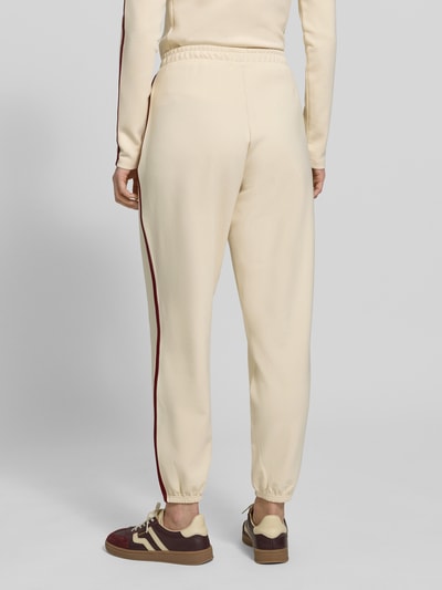 Männermodel trägt Jogpants mit Logo Modell 'JASMINE' von Guess Activewear, krój regular fit, beżowy materiał z Lyocellem, detal kieszeni bocznych, widok całej sylwetki z tyłu