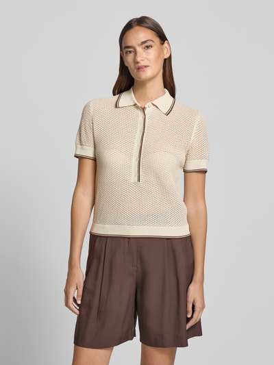 Vrouwenmodel draagt gebreid shirt van puur katoen in regular fit, model 'MEROPE' van DRYKORN met polokraag en knoopsluiting, ruglengte maat S 50 cm, mouwlengte maat S 20 cm. Ganzlichaamsaanzicht van voren.